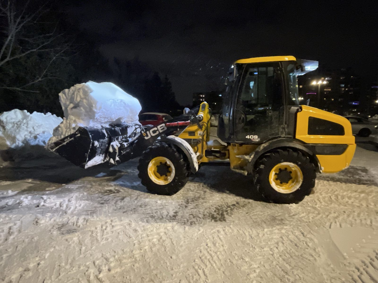 Loader carrying a full bucket of snow off a commercial lot